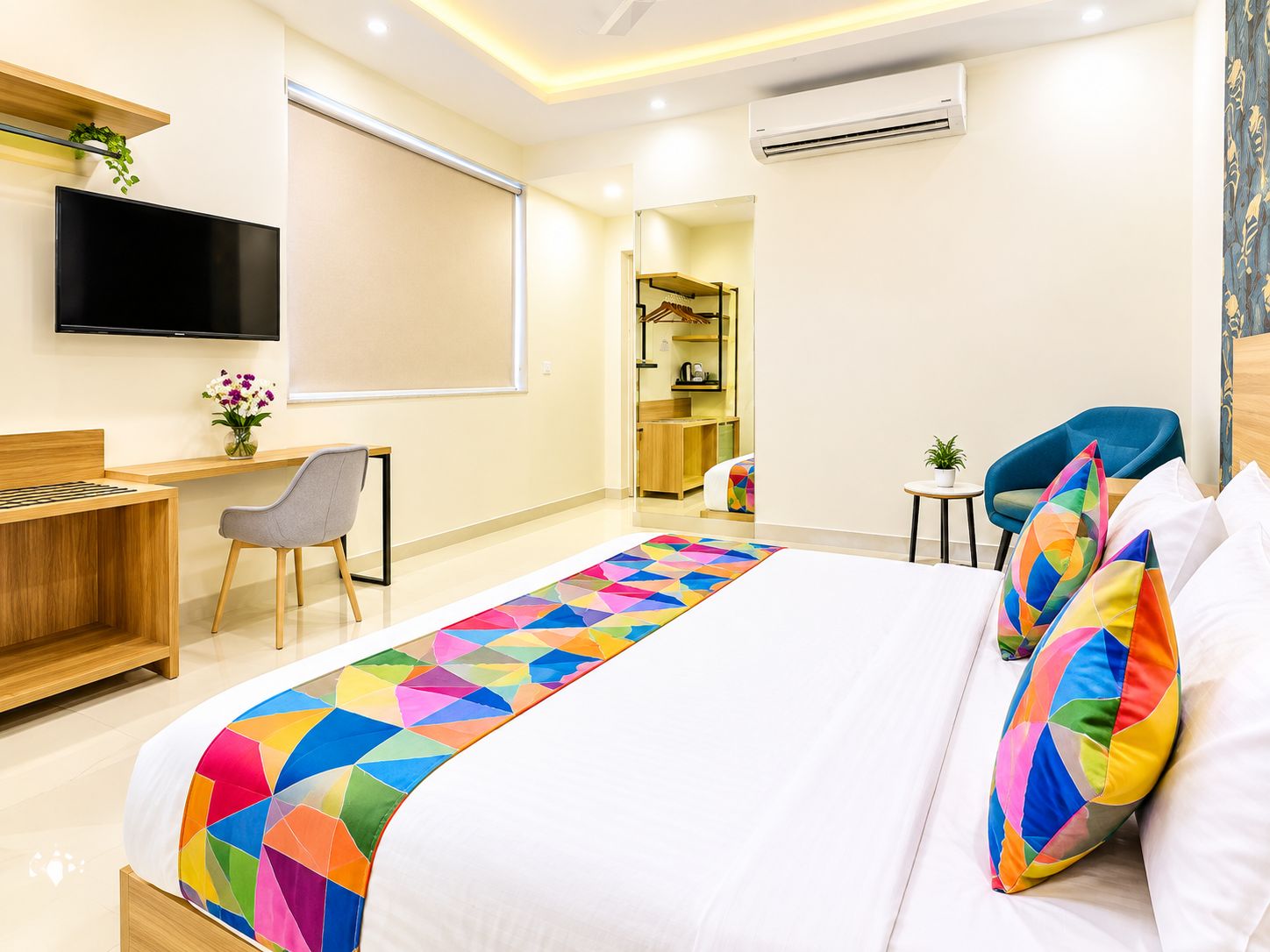 Habitación de hotel con cama, escritorio, silla, televisor y aire acondicionado.