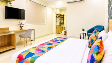 Habitación de hotel con cama, escritorio, silla, televisor y aire acondicionado.