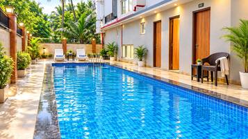 A swimming pool with a tiled edge, surrounded by potted plants and outdoor seating.