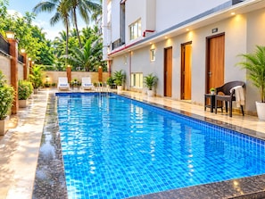 A swimming pool with a tiled edge, surrounded by potted plants and outdoor seating. - Hotel Twin Fountains - near Main Places (Calangute)