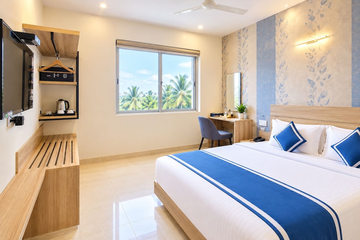 A hotel room with a bed, desk, chair, and a large window with a view of palm trees.