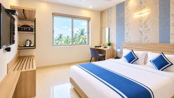 A hotel room with a bed, desk, chair, and a large window with a view of palm trees.