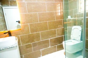 A bathroom with a glass partition, a white toilet, and a sink with a marble countertop. - Ken Kol Apartment  (Lekki)