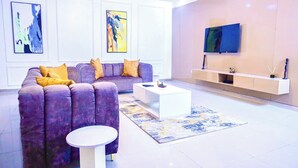 A modern living room with a purple sofa, a white coffee table, and a TV mounted on the wall. - Ken Kol Apartment  (Lekki)