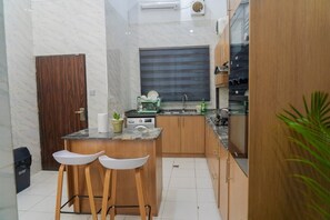 A compact kitchen with a marble backsplash, wooden cabinets, a built-in stove, and a small island with stools. - Ken Kol Apartment  (Lekki)
