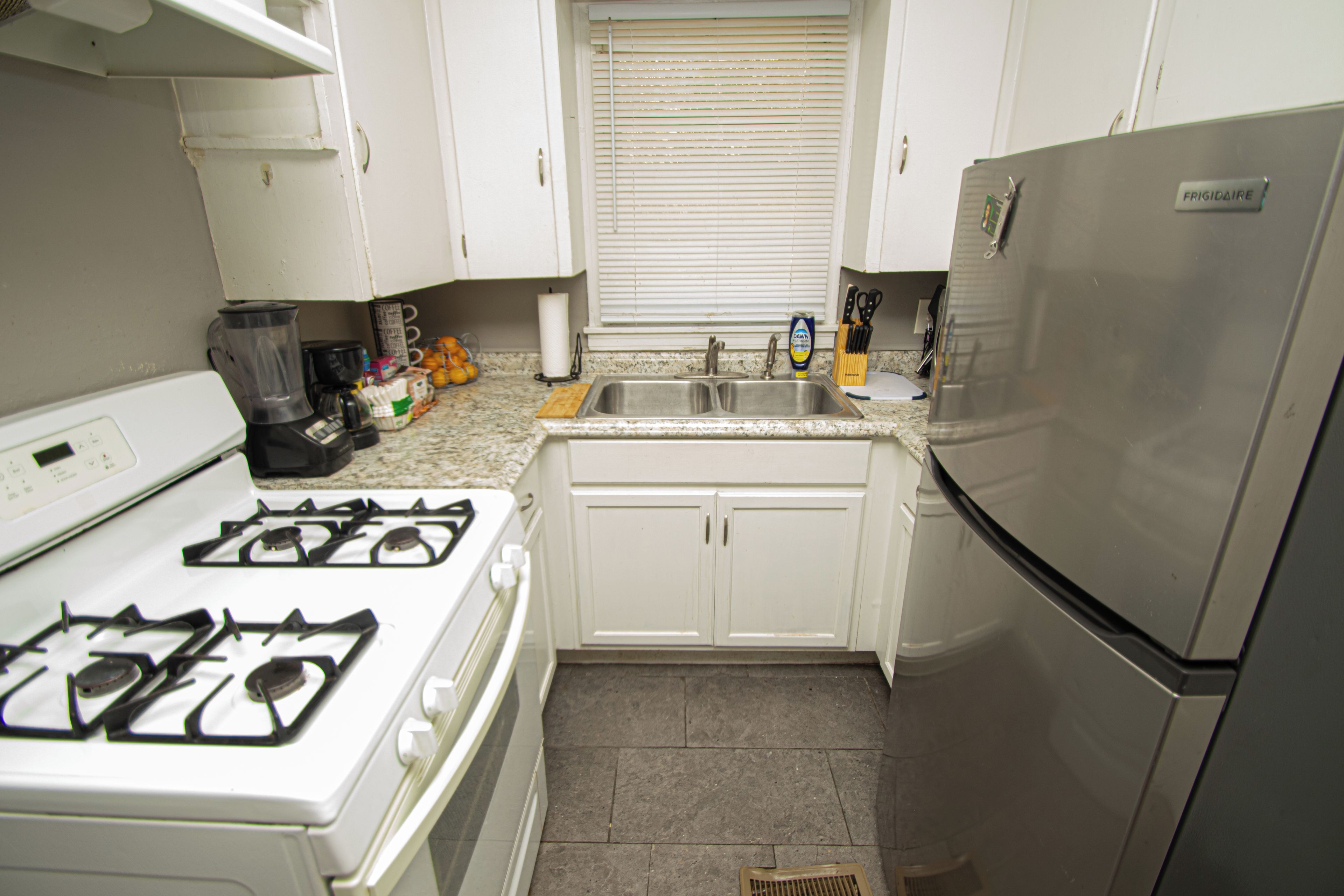 Una cocina con armarios blancos, un refrigerador de acero inoxidable, una estufa a gas y un lavaplatos.