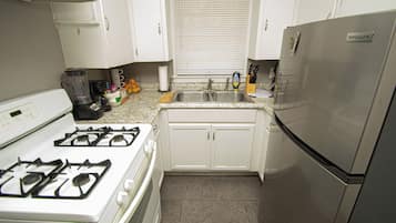 Una cocina con armarios blancos, un refrigerador de acero inoxidable, una estufa a gas y un lavaplatos.