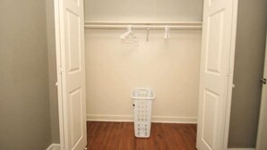 Un armario vestidor con piso de madera, una cesta blanca para ropa y una barra para colgar.