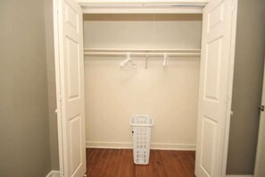 Un armario vestidor con piso de madera, una cesta blanca para ropa y una barra para colgar.