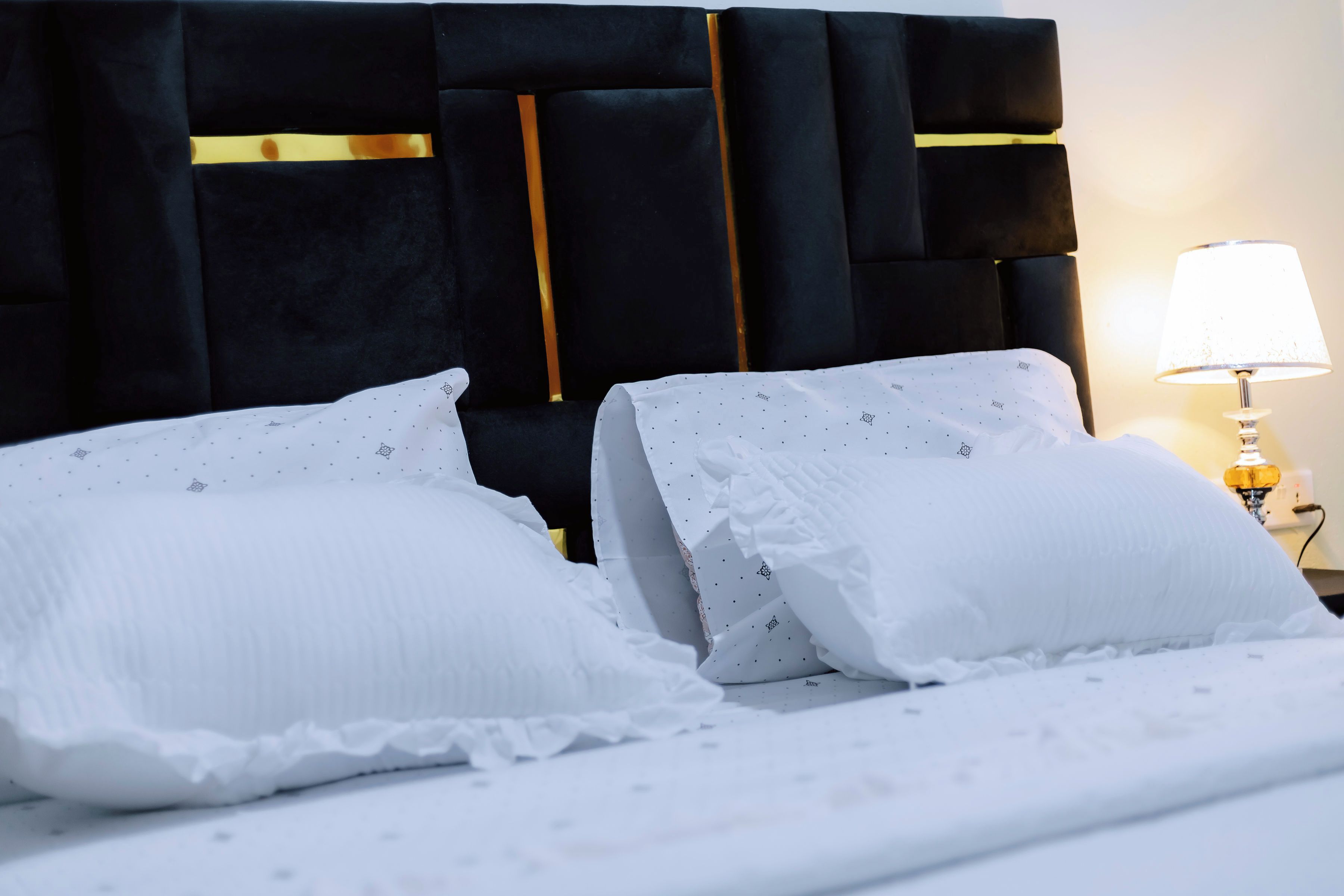 A bed with white bedding and a dark headboard with gold accents.