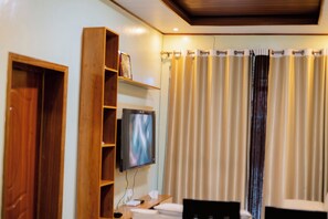 Una habitación de hotel con un armario de madera, un televisor montado en la pared, un escritorio con una silla y una cortina con diseño estampado.