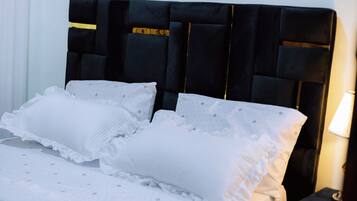 Una cama con cabecera tapizada de color negro, almohadas blancas y una colcha blanca con motivos pequeños.