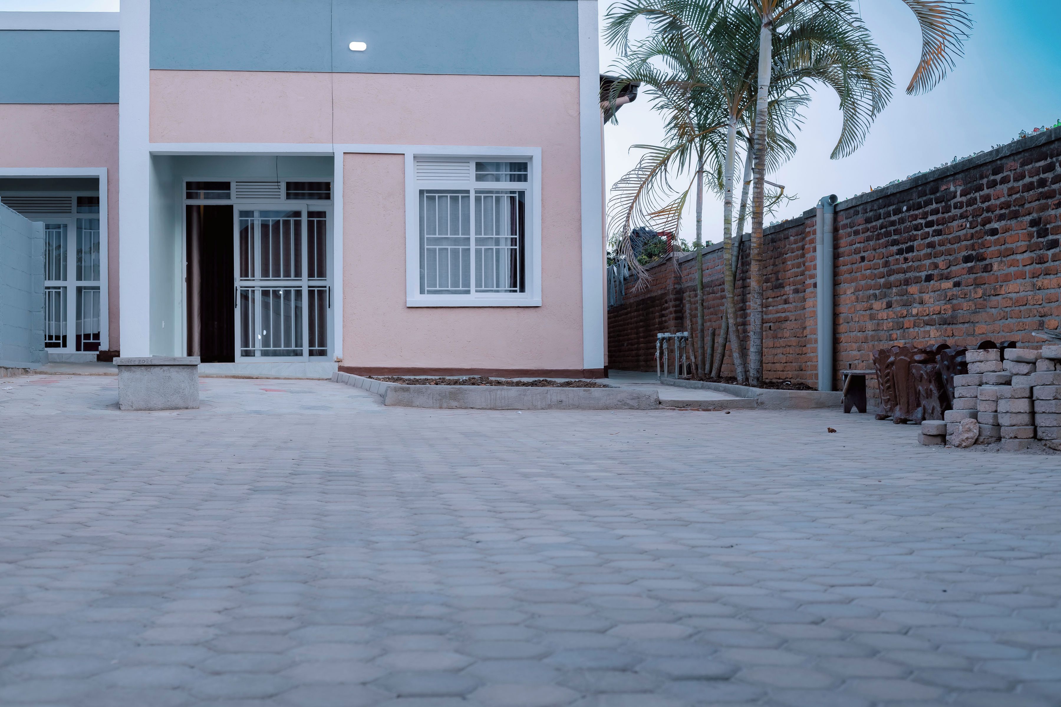 A building with a paved entrance area, a brick wall, and a palm tree.