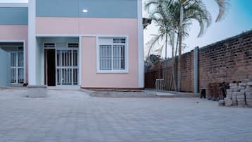 A building with a paved entrance area, a brick wall, and a palm tree.