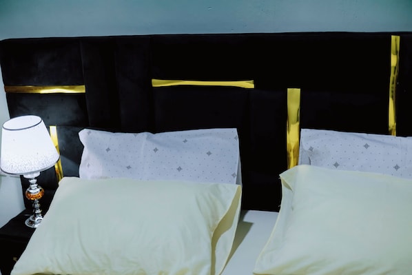 A hotel room with a black headboard, white pillows with a dotted pattern, and a bedside lamp.
