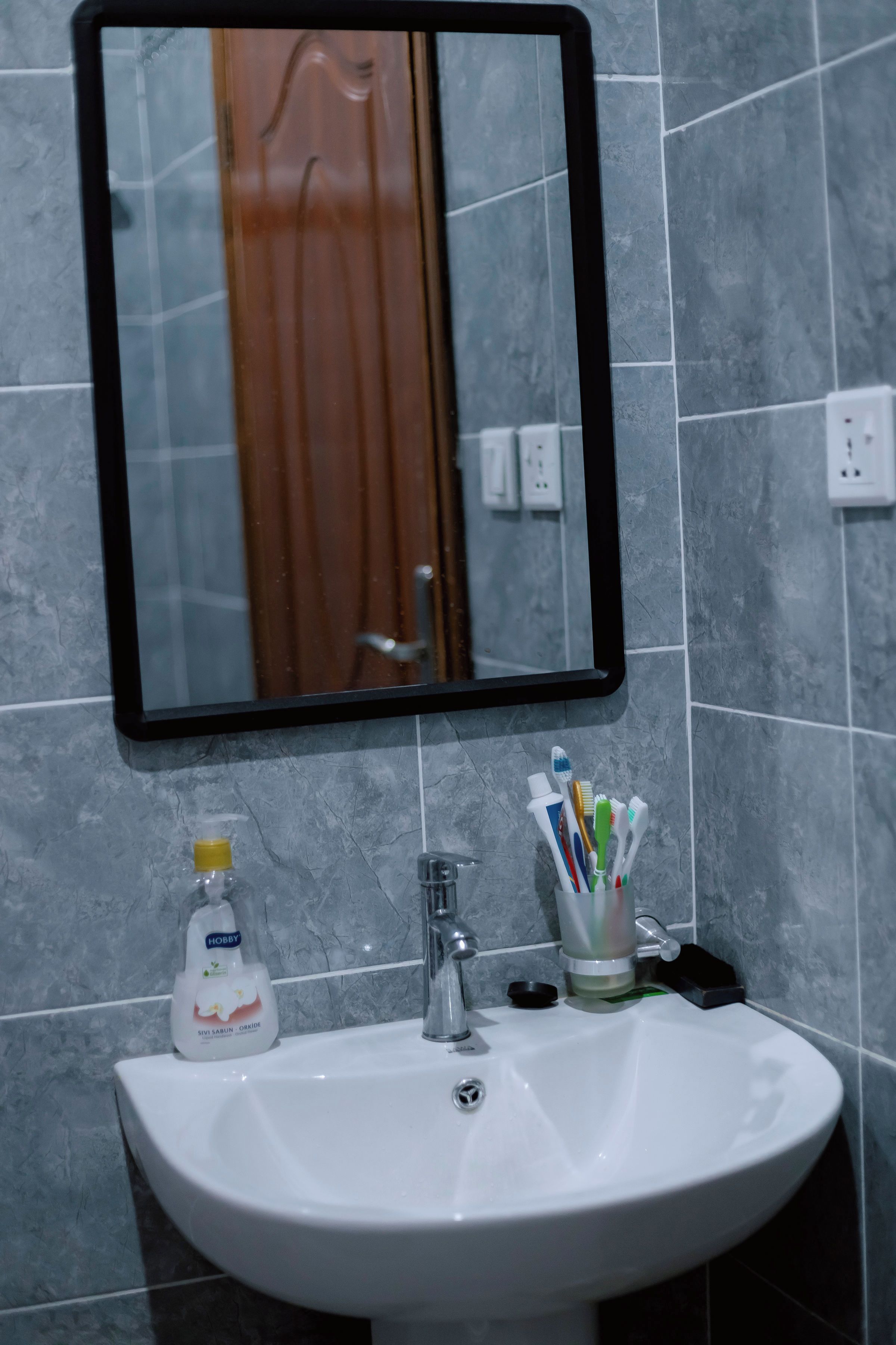 A bathroom sink with a mirror above it, a toothbrush holder with multiple toothbrushes, and a bottle of liquid soap.