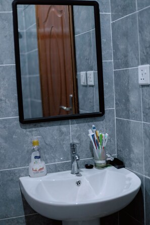 Ein Badezimmerwaschbecken mit Spiegel darüber, ein Zahnbürstenhalter mit mehreren Zahnbürsten und eine Flasche Flüssigseife.