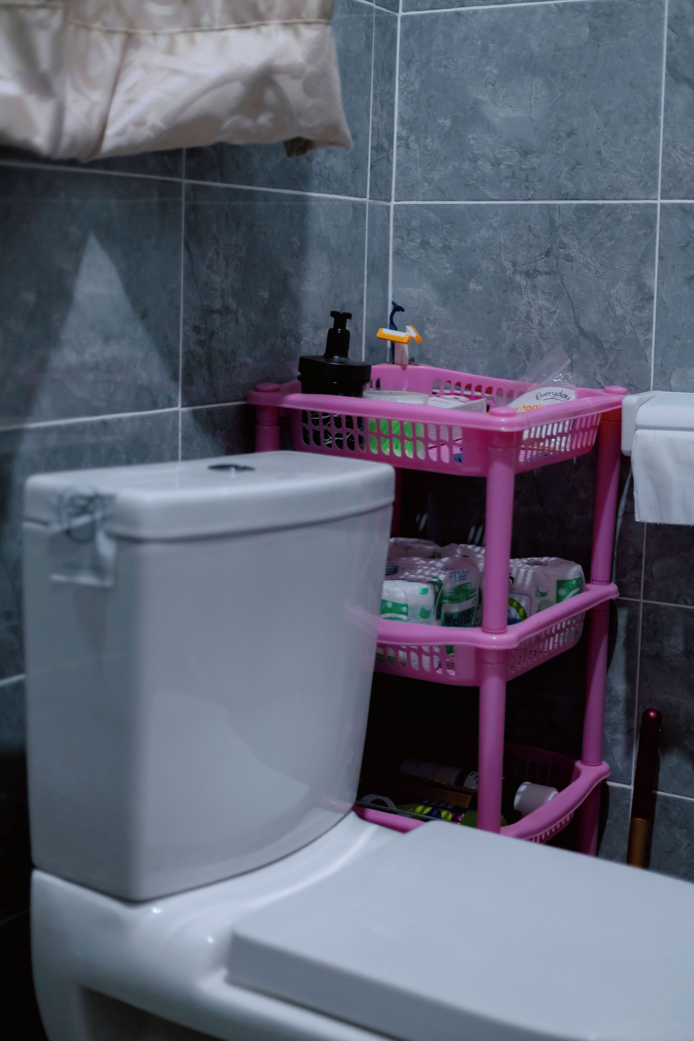 A bathroom with a white toilet, a pink basket with toiletries, and a towel hanging on the wall.
