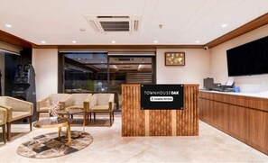 A reception area with a wooden reception desk, seating area with chairs and a coffee table, a television, and a large window. - Classic The Lake View Hotel (Durg)