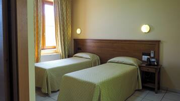 Habitación de hotel con dos camas individuales, una mesita de noche con teléfono y una ventana con cortinas.