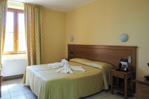 Una habitación de hotel con una cama, una mesita de noche con teléfono y una ventana con cortinas.