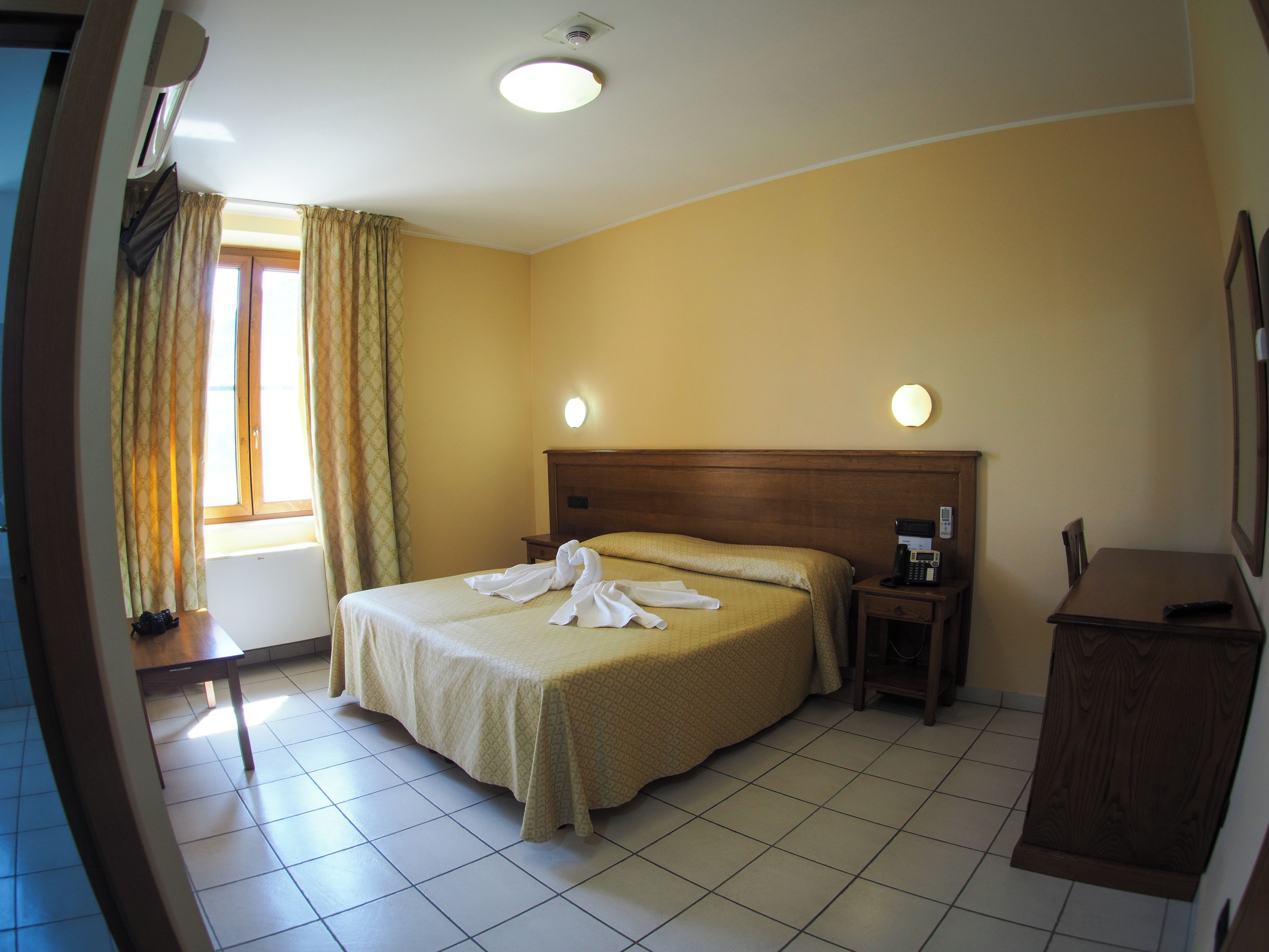 Una camera d'albergo con un letto, un comodino e un tavolino con il telefono.