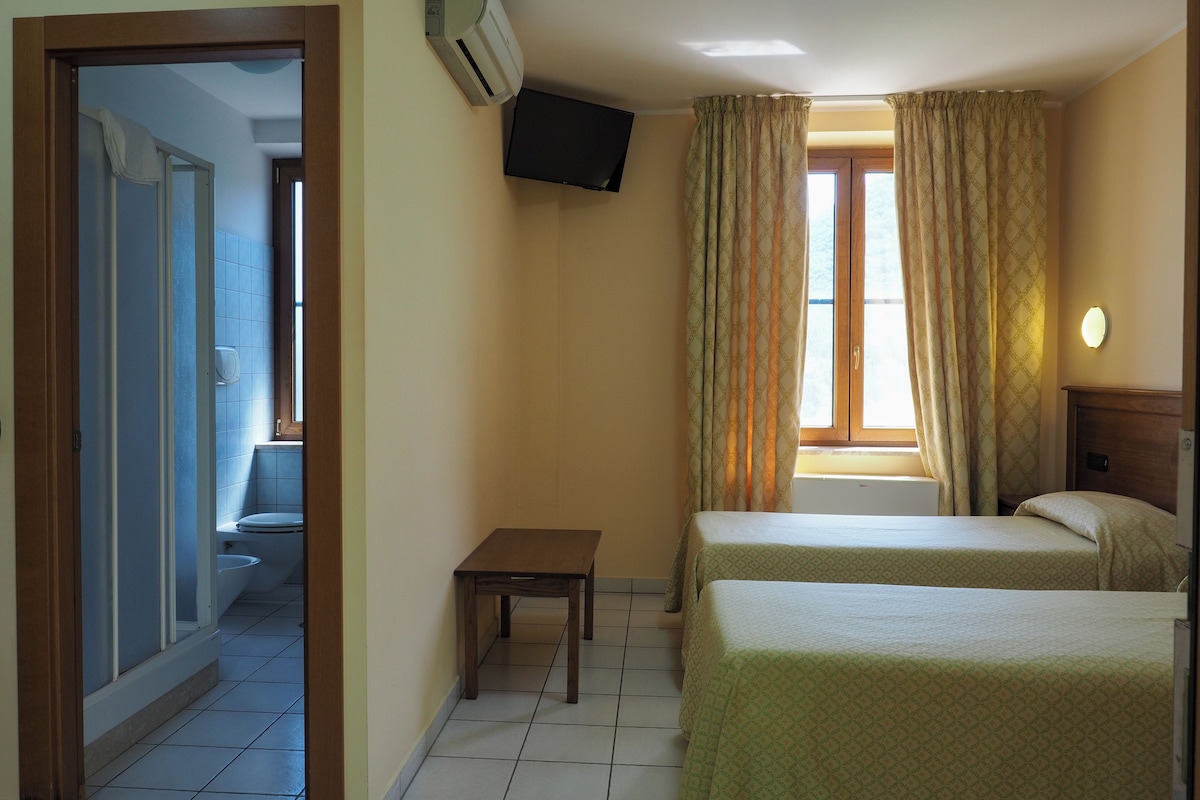 A hotel room with two beds, a television mounted on the wall, and a bathroom visible through an open door.