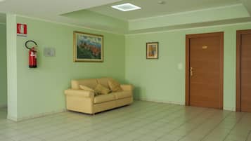 A room with a beige sofa, a painting, a fire extinguisher, and a door with a number plate.