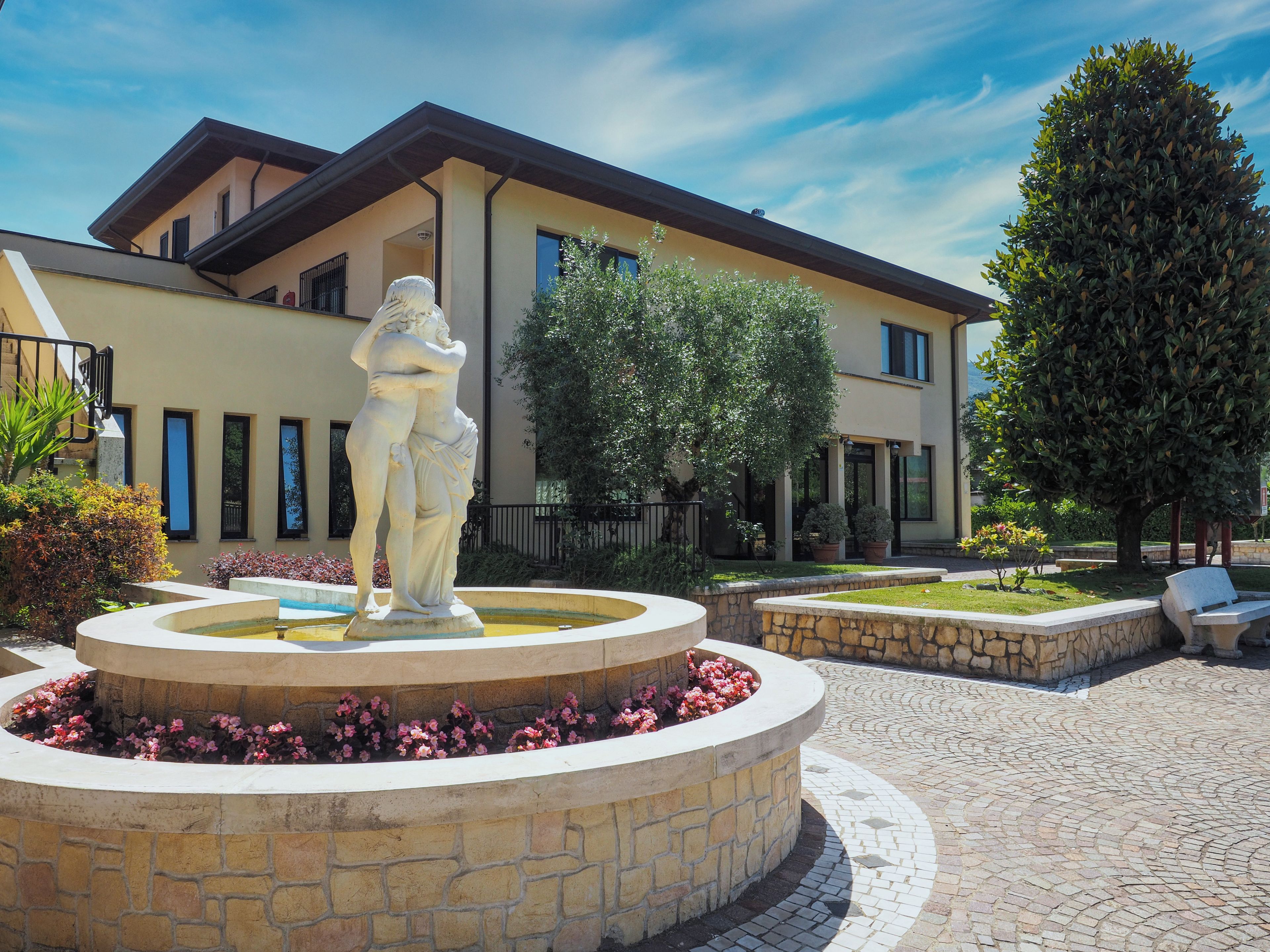 A courtyard with a central fountain, a statue, and a building with a balcony.