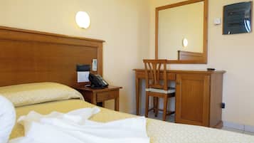 A hotel room with a bed, a desk, a chair, a telephone, a mirror, and a wall-mounted electrical panel.