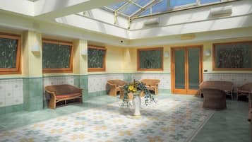 Una stanza luminosa con un pavimento decorato, mobili in vimini e un vaso centrale pieno di fiori.