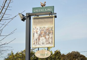 A sign for 'The Dog House' pub with a dog illustration and the name 'Greene King' above it.