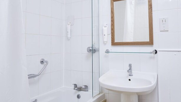 Un baño con cabina de ducha de vidrio, un lavabo blanco y un espejo con marco de madera.
