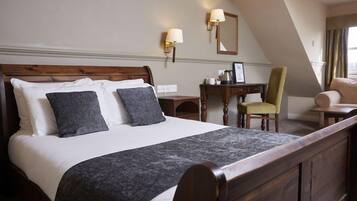 Habitación de hotel con una cama grande, un escritorio, dos sillas y un espejo en la pared.