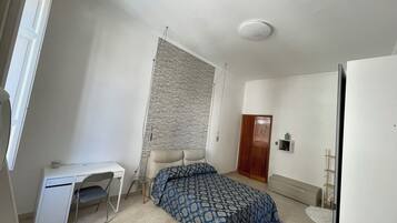 A bedroom with a bed, a desk, a chair, a wardrobe, and a radiator.