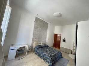 Un dormitorio con una cama, un escritorio, una silla, un armario y un radiador.