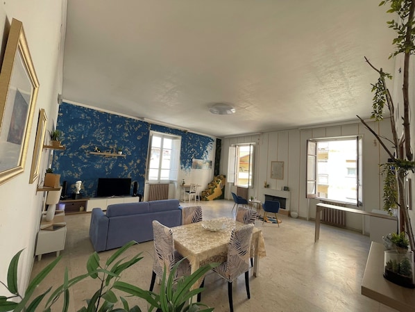 A living room with a blue wall, a sofa, a dining table with chairs, and a fireplace. - Vrbo Property (Lamezia Terme)