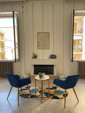 A room with a fireplace, two blue chairs, a small round table, and a patterned rug.