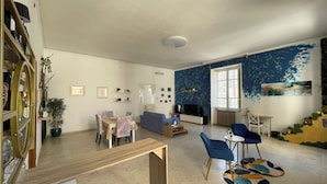 A spacious living room with a dining area, a blue sofa, a TV, and a staircase with a unique design. - Vrbo Property (Lamezia Terme)