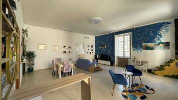 Un salon spacieux comprenant un coin repas, un canapé bleu, un téléviseur et un escalier au design original.