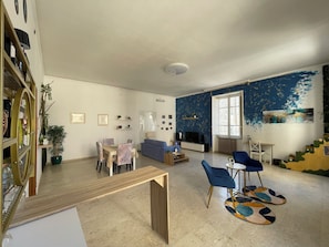 A spacious living room with a dining area, a blue sofa, a TV, and a staircase with a unique design. - Vrbo Property (Lamezia Terme)