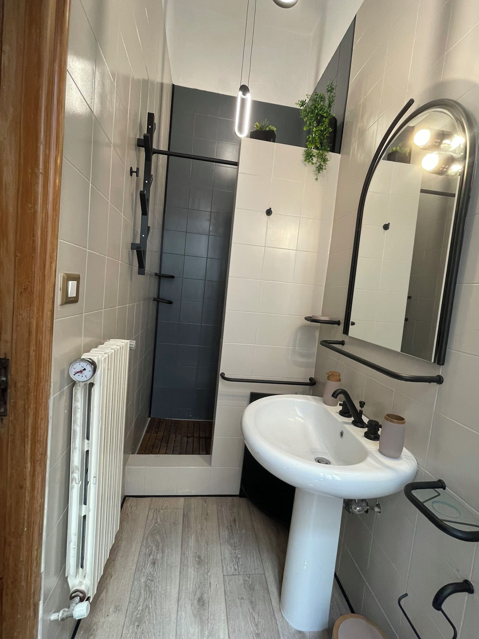 Un baño con lavamanos blanco, espejo, ducha con puerta de vidrio y radiador.
