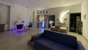 A spacious living area with a blue sofa, a coffee table, and a dining table with chairs. There is a kitchen area in the background with a refrigerator and a microwave. - Vrbo Property (Lamezia Terme)
