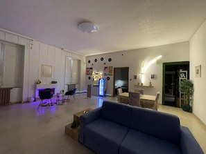 A spacious living area with a blue sofa, a coffee table, and a dining table with chairs. There is a kitchen area in the background with a refrigerator and a microwave. - Vrbo Property (Lamezia Terme)