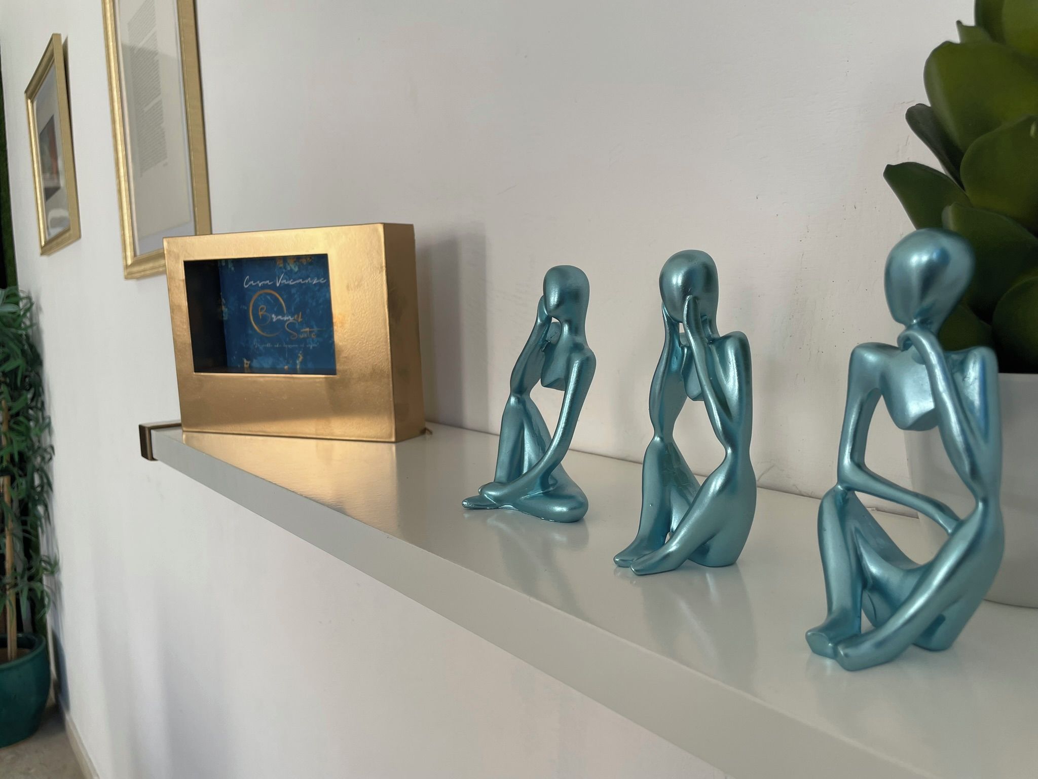 A shelf with a framed certificate, three metallic sculptures, and a potted plant.