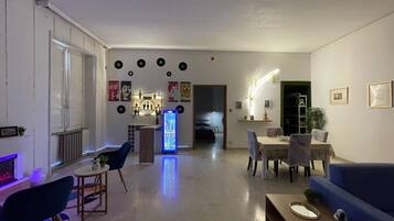 Un salon moderne avec un canapé bleu, une table basse, un coin repas avec une table et des chaises, un réfrigérateur et, au fond, un espace cuisine.