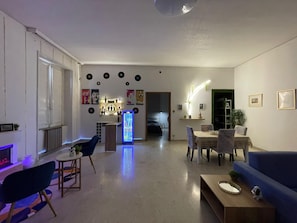 A modern living room with a blue sofa, a coffee table, a dining area with a table and chairs, a refrigerator, and a kitchen area in the background. - Vrbo Property (Lamezia Terme)