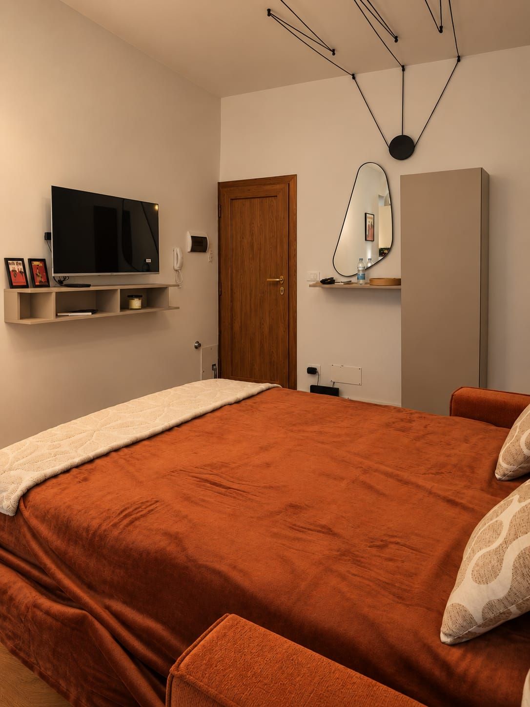 A bedroom with a large bed, a television mounted on the wall, a door, and a mirror.