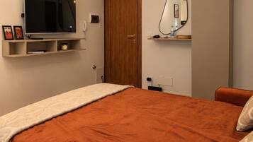 A bedroom with a large bed, a television mounted on the wall, a door, and a mirror.