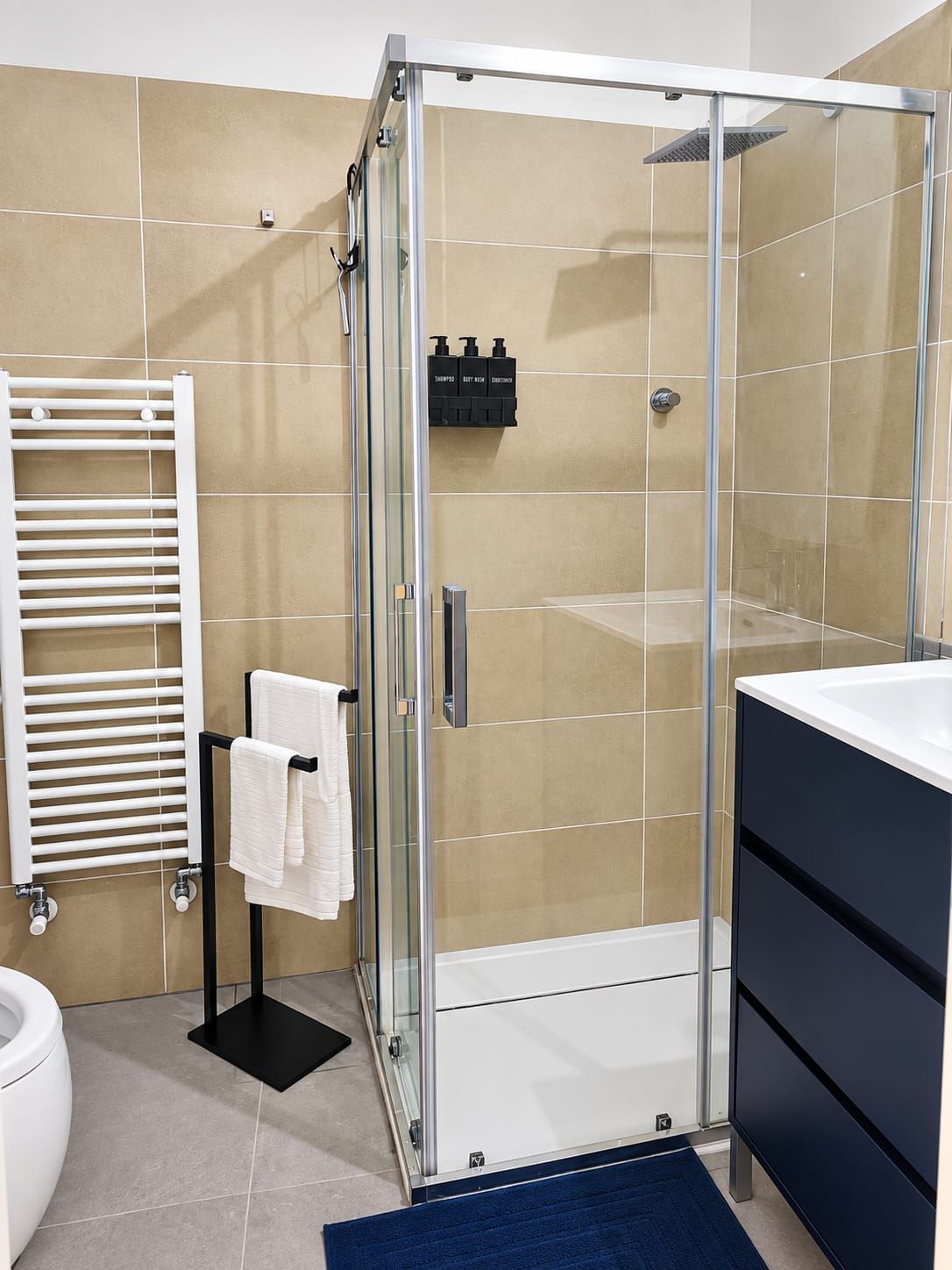A modern bathroom with a glass-enclosed shower, a white towel rack, and a black cabinet.